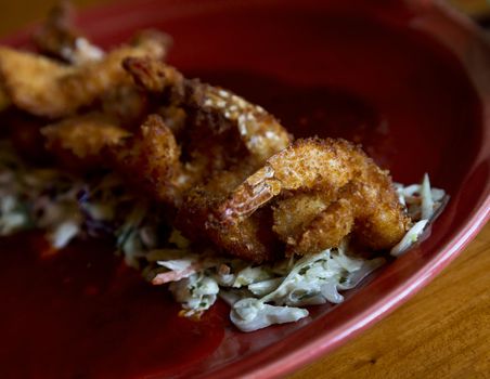Crispy fried shrimp placed atop shredded cabbage  on red plate. Wood grain table is rustic.  Red plate reflects modern Southwestern cuisine style.