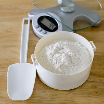 Bread flour in white bowl with rubber scraper and scale on wood table ready to baking bread