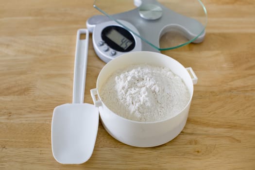 Bread flour in white bowl with rubber scraper and scale on wood table ready to baking bread