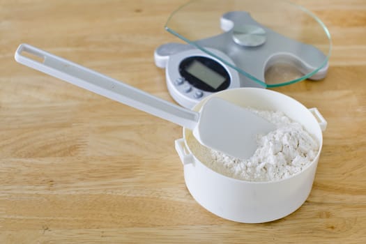 Bread flour in white bowl with rubber scraper and scale on wood table ready to baking bread