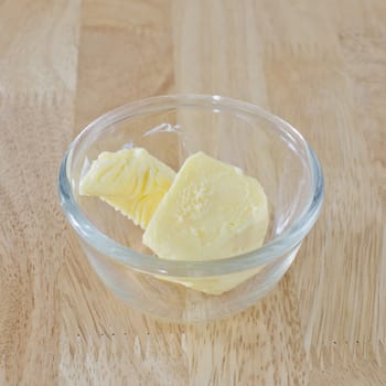 Stick of butter, cut, in glass bowl on wood table.