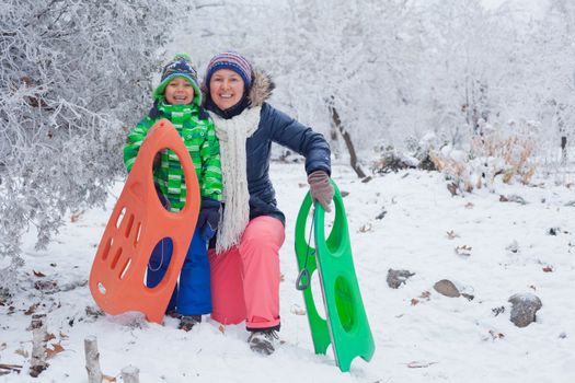 Winter, play, fun - Mother and her cute little son having fun with sled in winter park