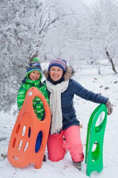 Winter, play, fun - Mother and her cute little son having fun with sled in winter park