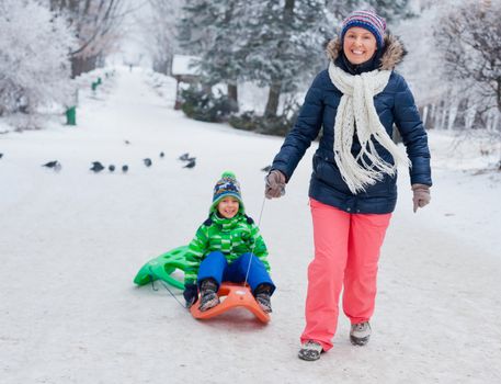 Winter, play, fun - Mother and her cute little son having fun with sled in winter park