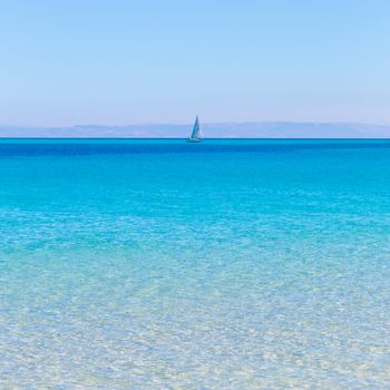 White sail boat at the beautiful turquoise blue mediterranean Pelosa beach near Stintino,Sardinia, Italy.