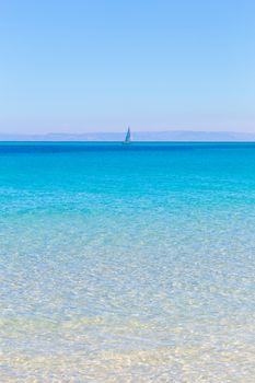 White sail boat at the beautiful turquoise blue mediterranean Pelosa beach near Stintino,Sardinia, Italy.