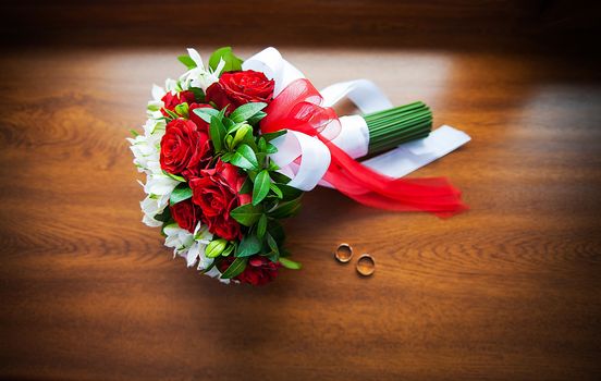 Beautiful wedding bouquet and rings on wood background.