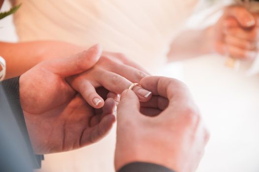 groom putting on wedding ring on bride's finger 