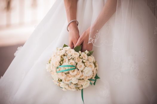 bride holding wedding bouquet from white roses with green ribbon