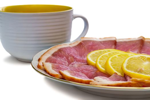Delicious slices of ham and lemon to the dish and a big Cup. Presented on a white background.
