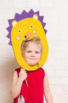 Little blonde girls holding hedgehog mask on white background