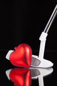 Golf putter and red heart on the black glass desk