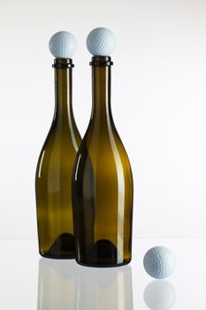 Empty two wine bottles and golf balls on a glass desk