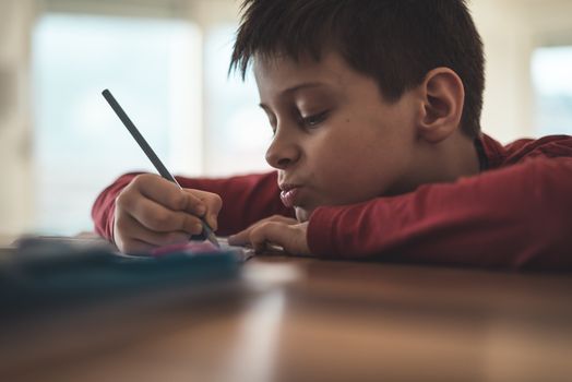 Boy writing homework reluctantly at home
