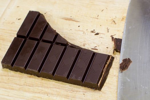 Cut Chocolate bars and knife on a wooden cutting board