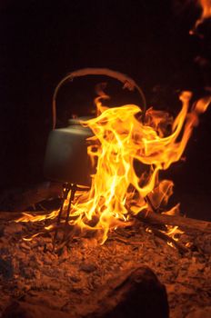 Camp kettle on a burning campfire at night.