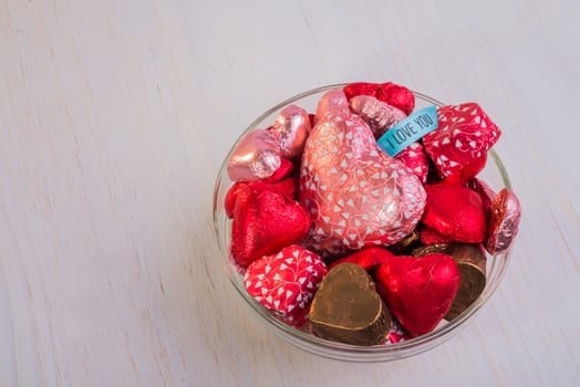A glass bowl filled with heart shaped chocolates.