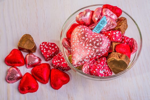 A glass bowl filled with heart shaped chocolates.