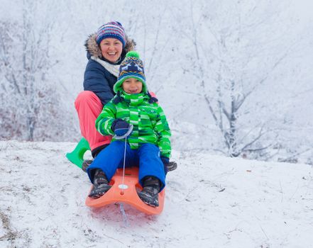 Winter, play, fun - Mother and her cute little son having fun with sled in winter park