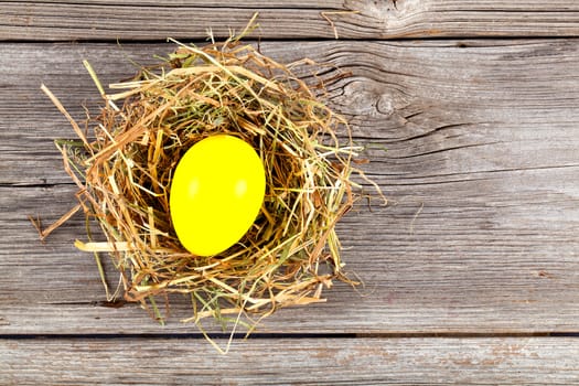 yellow easter egg in nest on vintage wooden background