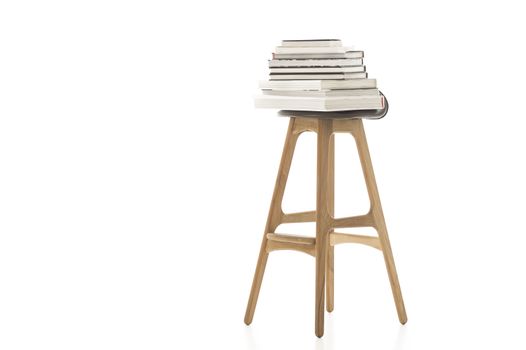 Conceptual Pile of Books on Top of Wooden Leg Chair Isolated on White Background. Emphasizing White Background.