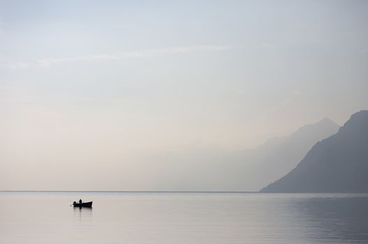A lone boat on the horizon of the vast of the lake Garda in the northern Italy with light blue morning skies and disappearing mountains in the background.