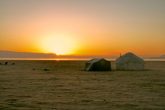 Sun rising over traditional yurt of nomadic tribe on green grasslands in Kyrgyzstan