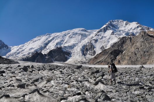 Young adventurer with backpack on glacier below snow-covered highest peaks in Tien-Shan mountain range in Kyrgyzstan