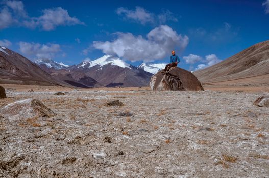 Young hiker sitting on the rock high in Pamir mountains in Tajikistan