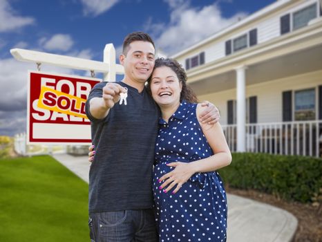 Happy Hispanic Couple In Front of New Home And Sold Real Estate Sign Showing Off Their House Keys.