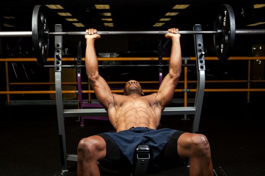 Weight lifter at the bench press lifting a barbell on an incline bench.