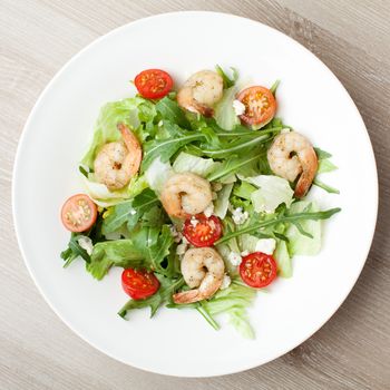 Fresh gourmet seafood salad with lettuce, rocket and corn greens, shrimps, cherry tomatoes, cheese  served in white plate