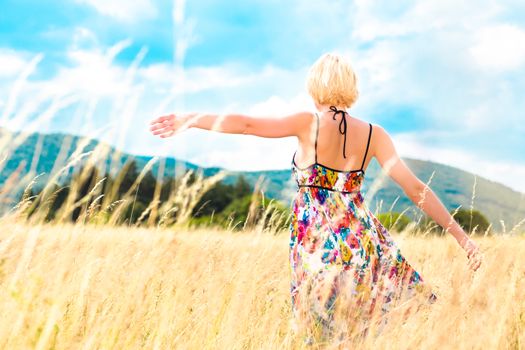 Lady enjoying the nature. Young woman arms raised enjoying the fresh air in summer meadow.