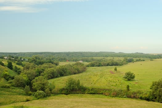 Green meadows near small river with blue sky and forest horizontal