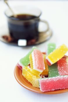 fruit jellies are in a saucer, near a cup with tea