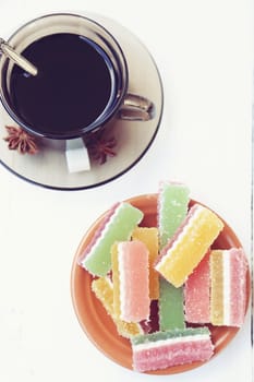 fruit jellies are in a saucer, near a cup with tea