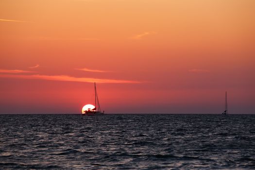 two sailboats over orange sunset at open sea. One of the boats is in the sun