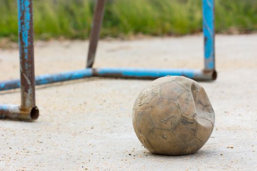 old soccer ball on concrete field with old blue goal