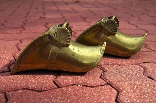 A pair of gold gaucho stirrups against a brick walk