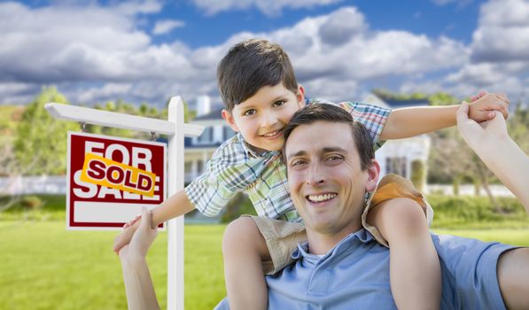 Mixed Race Father and Son Celebrating with a Piggyback in Front Their House and Sold Real Estate Sign.