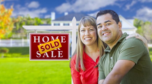 Happy Mixed Race Couple in Front of Sold Home For Sale Real Estate Sign and House.