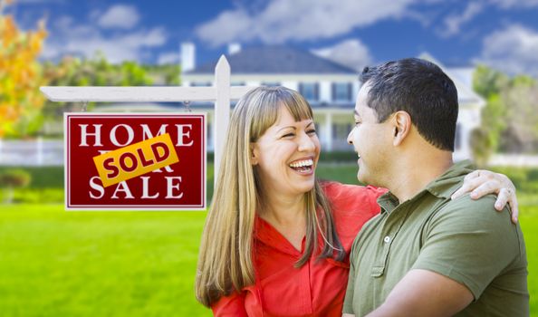 Happy Mixed Race Couple in Front of Sold Home For Sale Real Estate Sign and House.