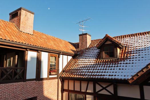 Tiled roof of a european house with chimney, antenna and snow at sunset