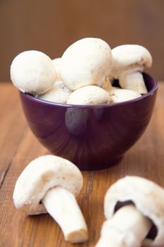 many raw fresh mushrooms in a bowl on a wooden background