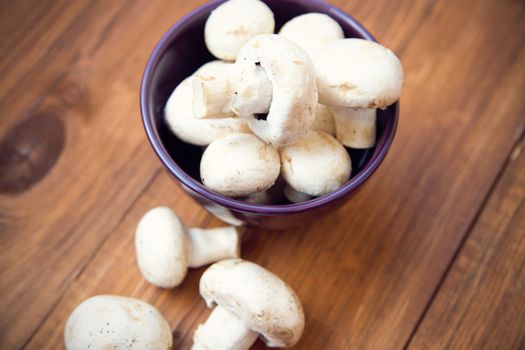 many raw fresh mushrooms in a bowl on a wooden background