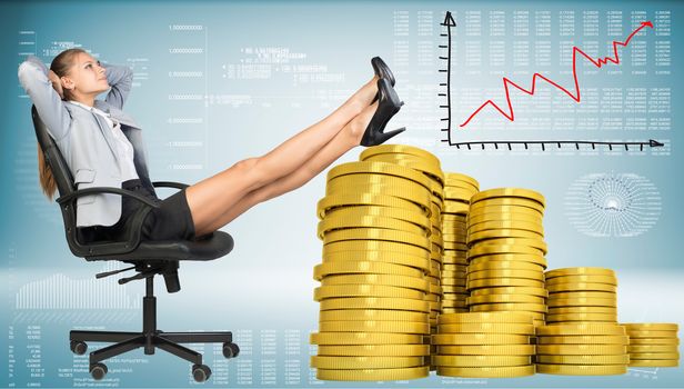 Businesswoman smiling sitting on office chair with her hands behind her head and her feet up on piles of golden coins. Graph showing growth beside. Hi-tech charts with various data as backdrop