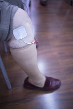 Female patient knee, leg, thigh and calf in physiotherapy rehabiliation treatment from injury in hospital clinic with electrical stimulus attached with plaster.