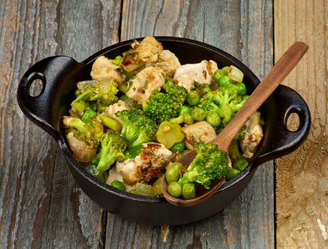 Black Saucepan with Homemade Chicken Stew with Broccoli, Bell Pepper and Green Pea closeup on Rustic Wooden background