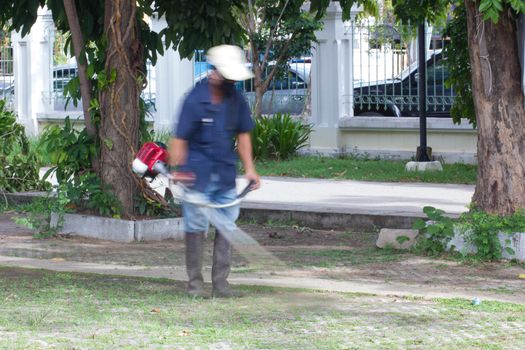 Blurred image of a man mowing the grass in public park
