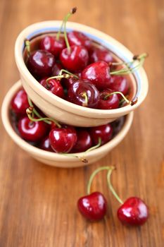 many ripe raw wet sweet cherry in dish on wooden background